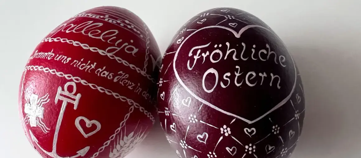Zwei bemalte Ostereier: Ein rotes mit "Halleluja" und Anker, ein dunkles mit "Fröhliche Ostern" und Herzen. Ein schöner risus paschalis.