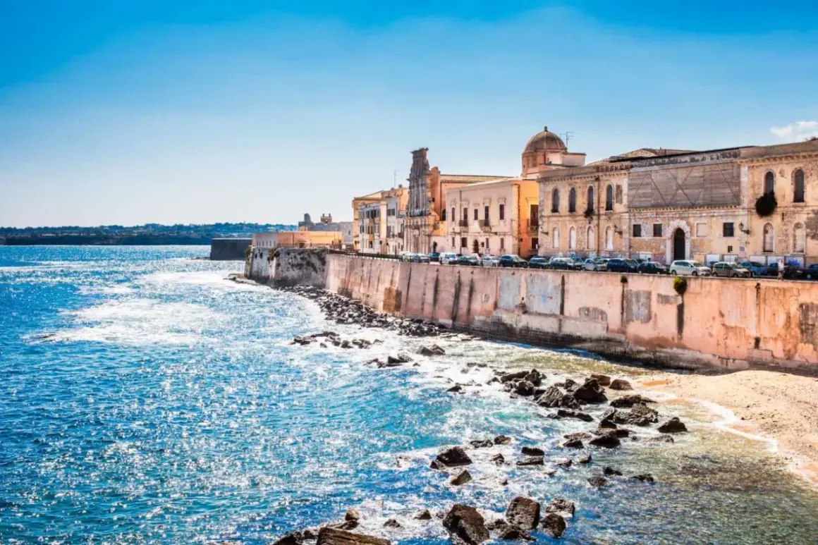 Costa de Siracusa, Sicilia, con edificios históricos y el mar azul brillante.
