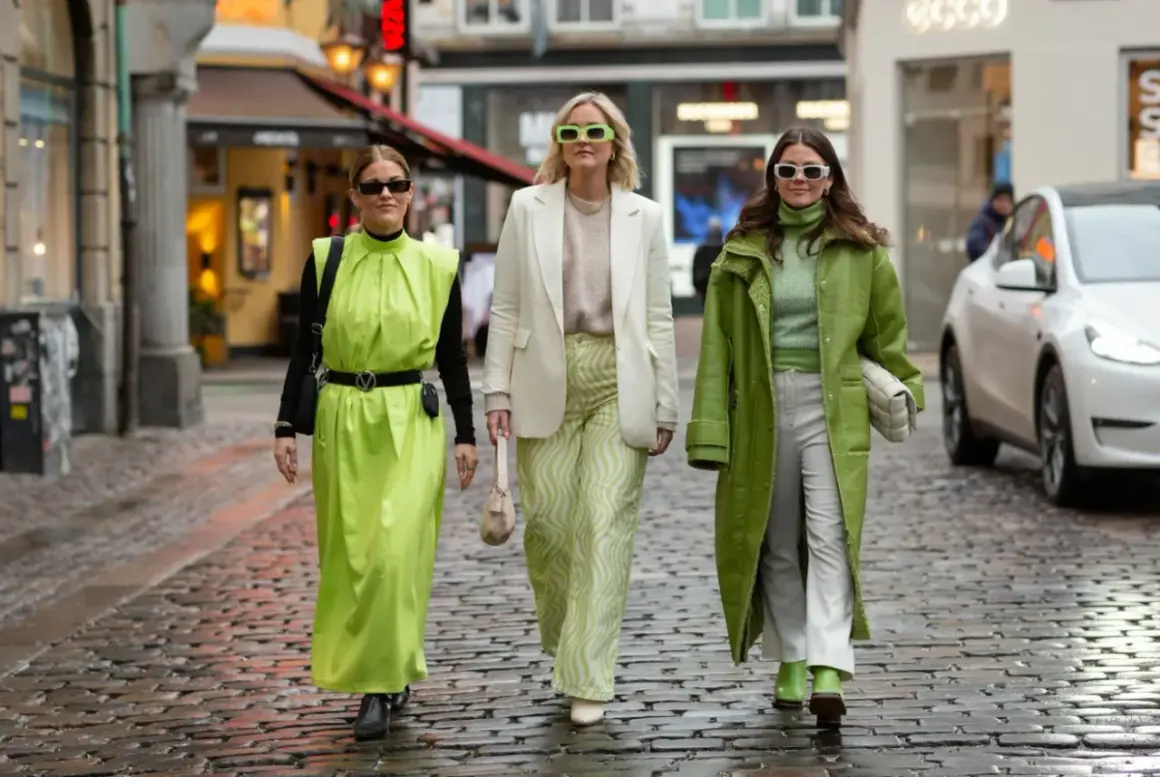 Tre kvinnor i ljusgröna och vita kläder, med solglasögon, promenerar på en kullerstensgata. En tydlig dansk kvinna stil.
