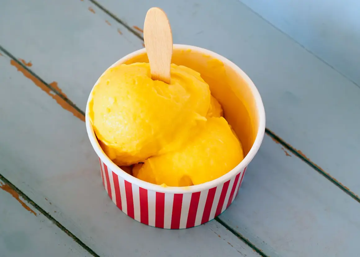 Un refrescante helado de mango en un recipiente a rayas rojas y blancas, listo para disfrutar en un día caluroso.