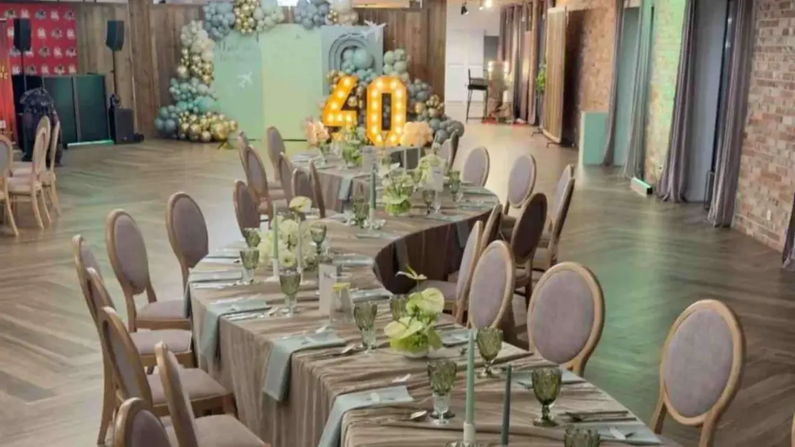 Eleganckie przyjęcie weselne na 40 osób. Stoły nakryte, ozdobione kwiatami i świecami. W tle dekoracje z balonów i podświetlana liczba 40.