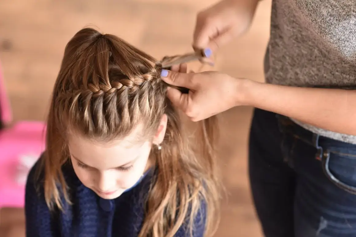 Bambina con capelli castani corti e trecce a cascata. Le mani di una persona le stanno creando una nuova treccia.