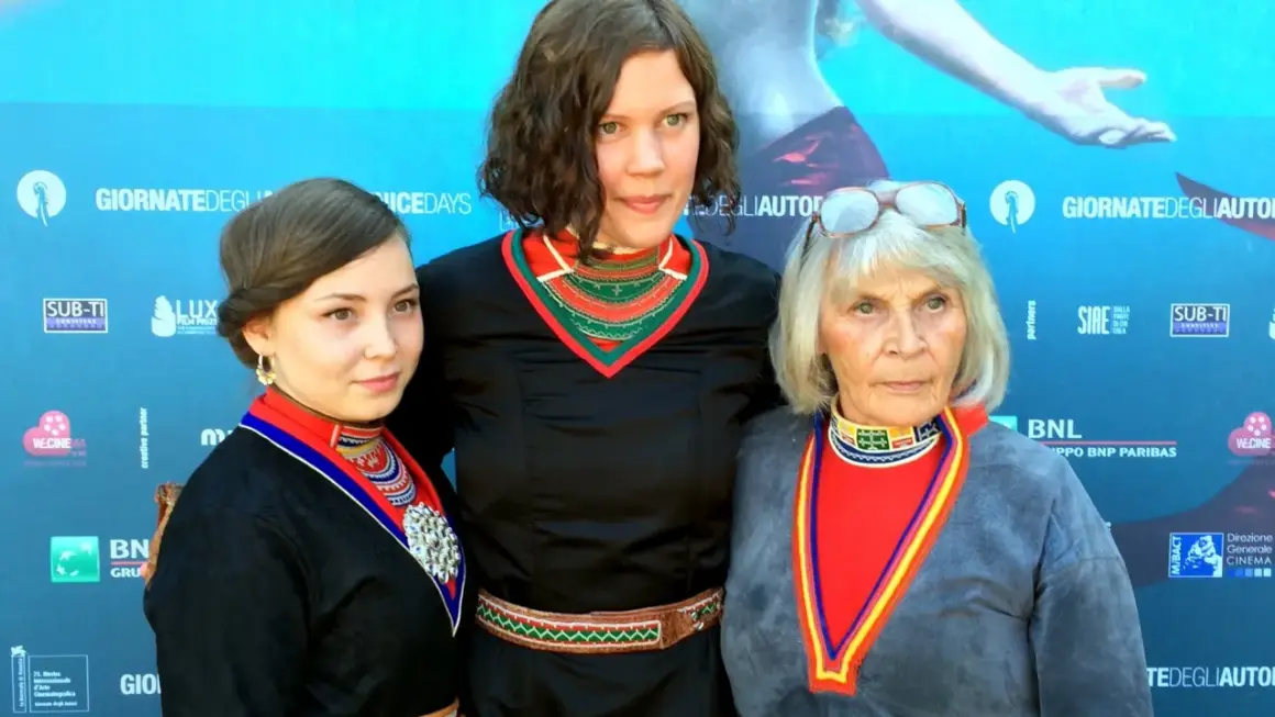Tre kvinnor i traditionella samiska dräkter poserar framför en blå bakgrund med logotyper. De representerar en stark berättelse, likt den i feministiska filmer.