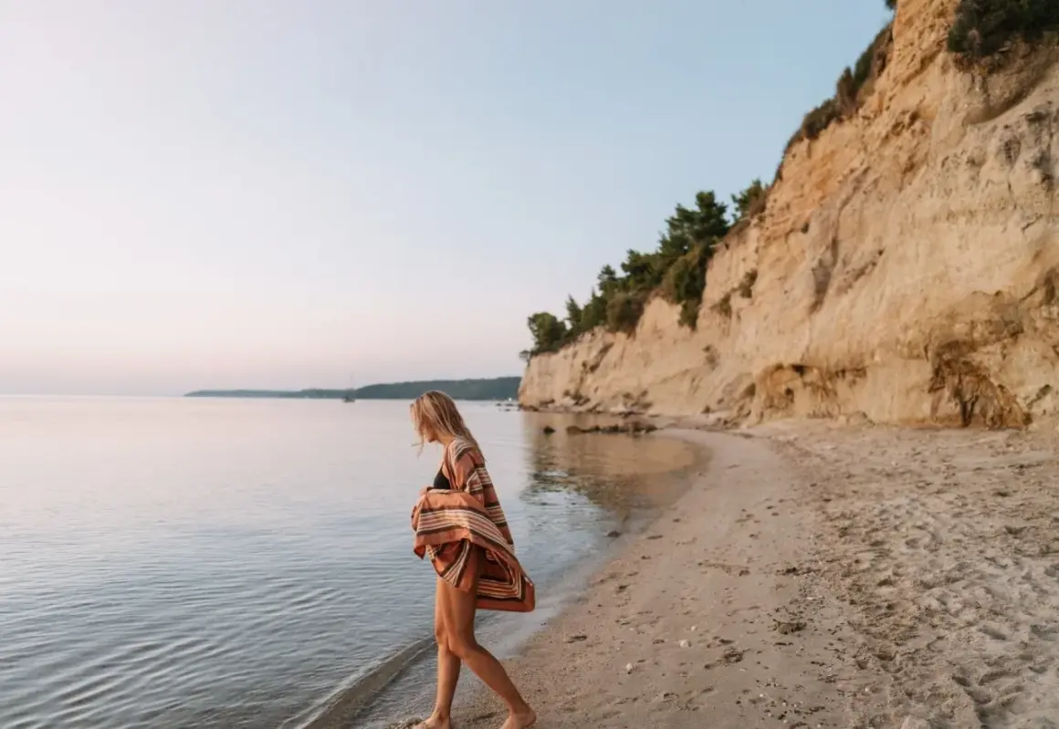 Mujer rubia camina por la playa, sintiendo la brisa marina. Ella anhela la libertad y el deseo de querer viajar sola.