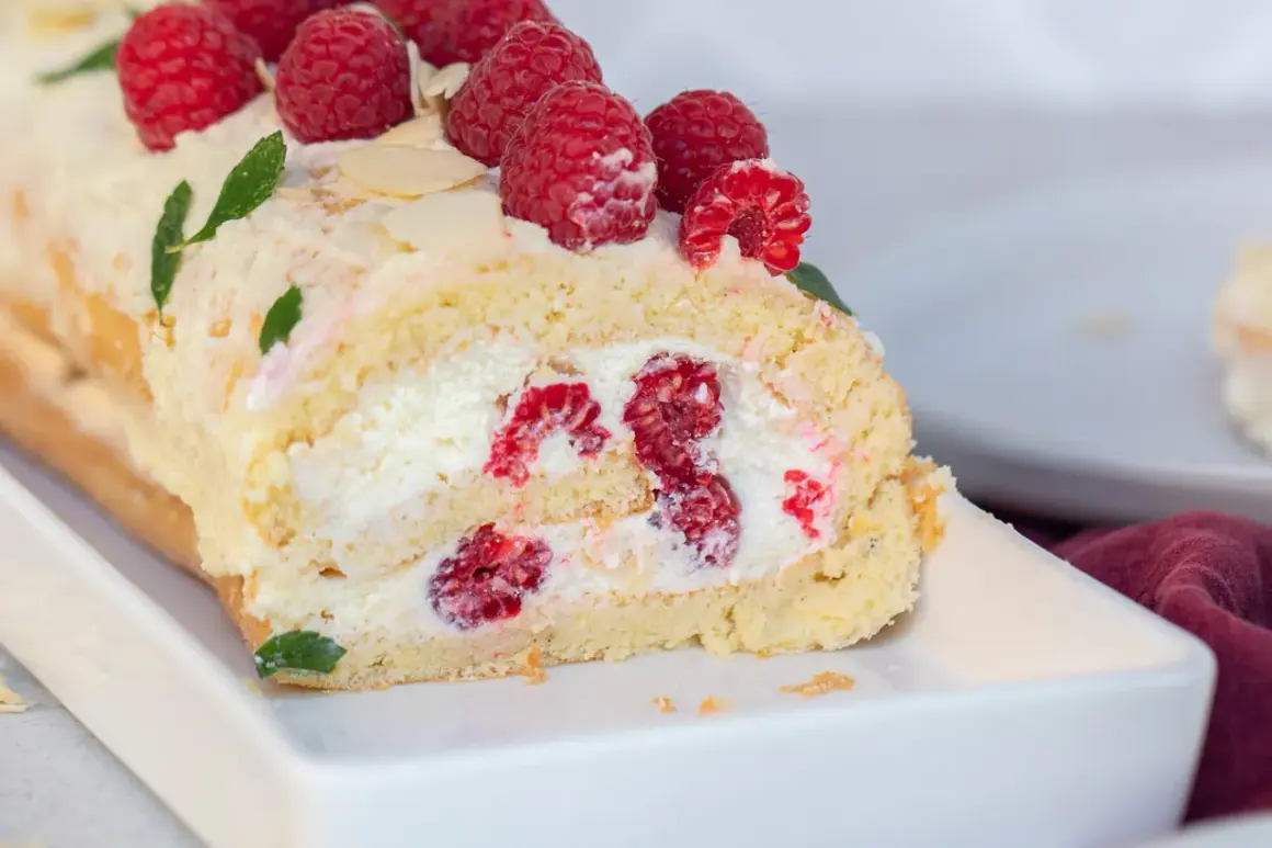 Saftige Biskuitrolle mit frischen Himbeeren und Sahne gefüllt, garniert mit Beeren und Mandelblättchen. Ein Genuss!