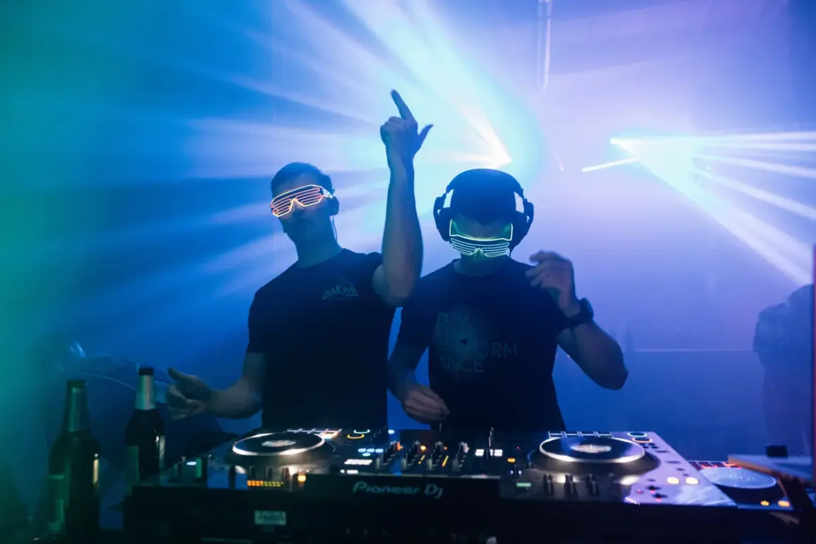 Dwóch DJ-ów w neonowych okularach gra muzykę trance na imprezie z laserami.