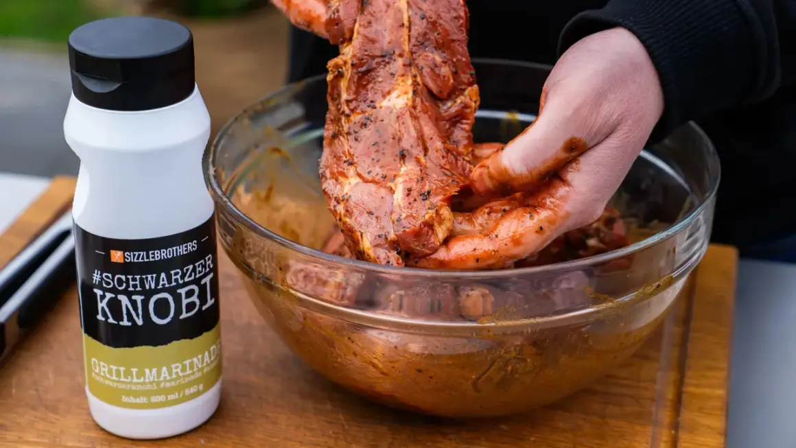 Fleisch wird mit einer würzigen Grillmarinade in einer Schüssel vermischt. Die Flasche "#Schwarzer Knobi" zeigt, wie einfach es ist, Grillmarinade selber machen.
