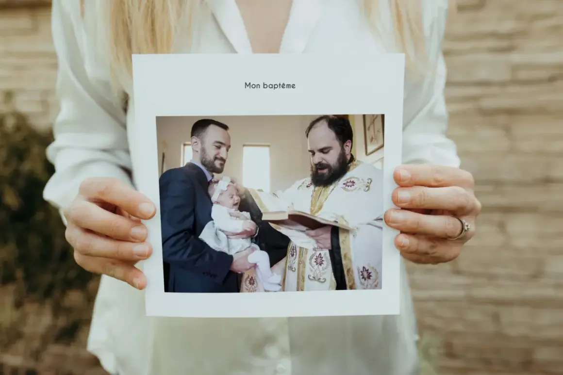 Carte "Mon baptême" tenue par des mains. Photo d'un bébé pleurant, tenu par son père, recevant le baptême d'un prêtre. Un beau texte baptême pour les grands-parents.