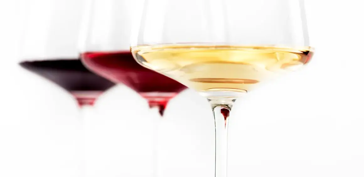 Trzy kieliszki z winem: ciemnoczerwonym, rubinowym i białym. Wino się pieni, tworząc subtelne refleksy.