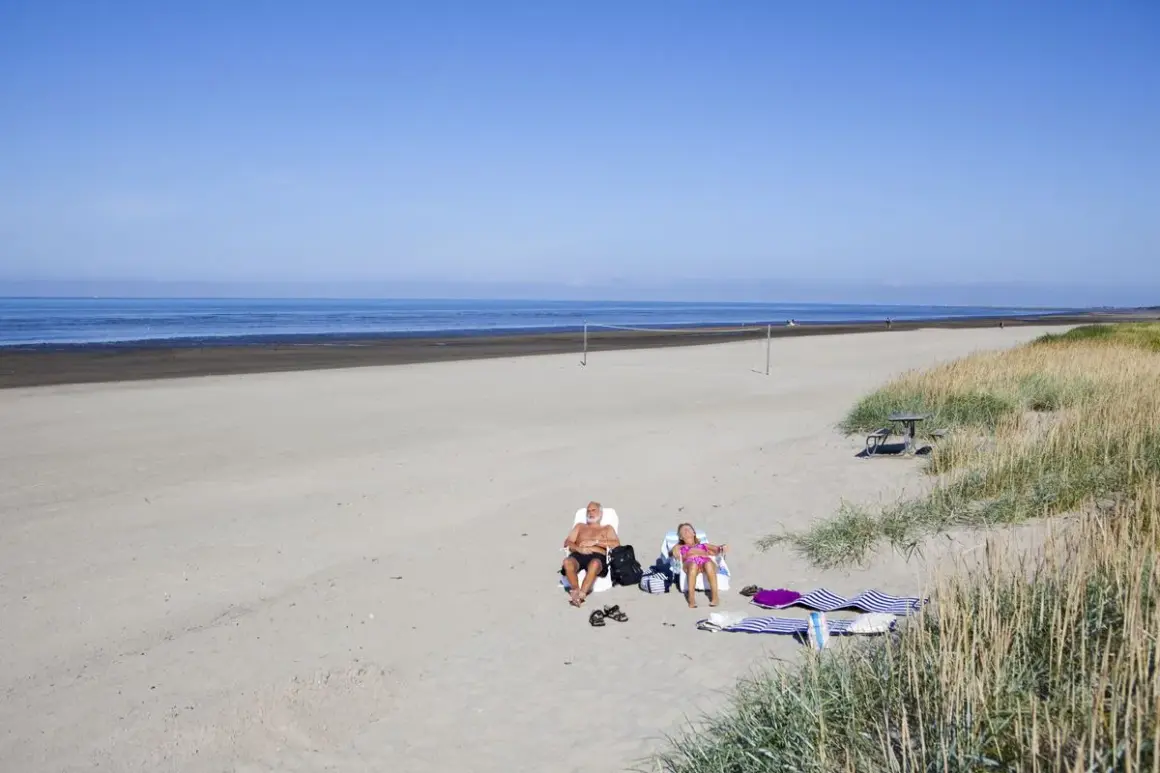 Två personer solar på stranden vid Björkäng camping. En man och en flicka njuter av solen.