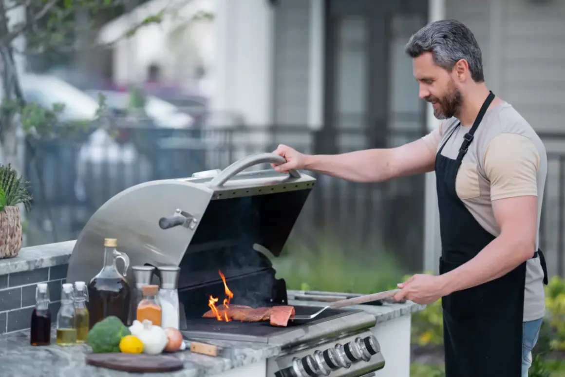 Mężczyzna w fartuchu grilluje łososia na grillu gazowym, pokazując, jak działa grill gazowy.