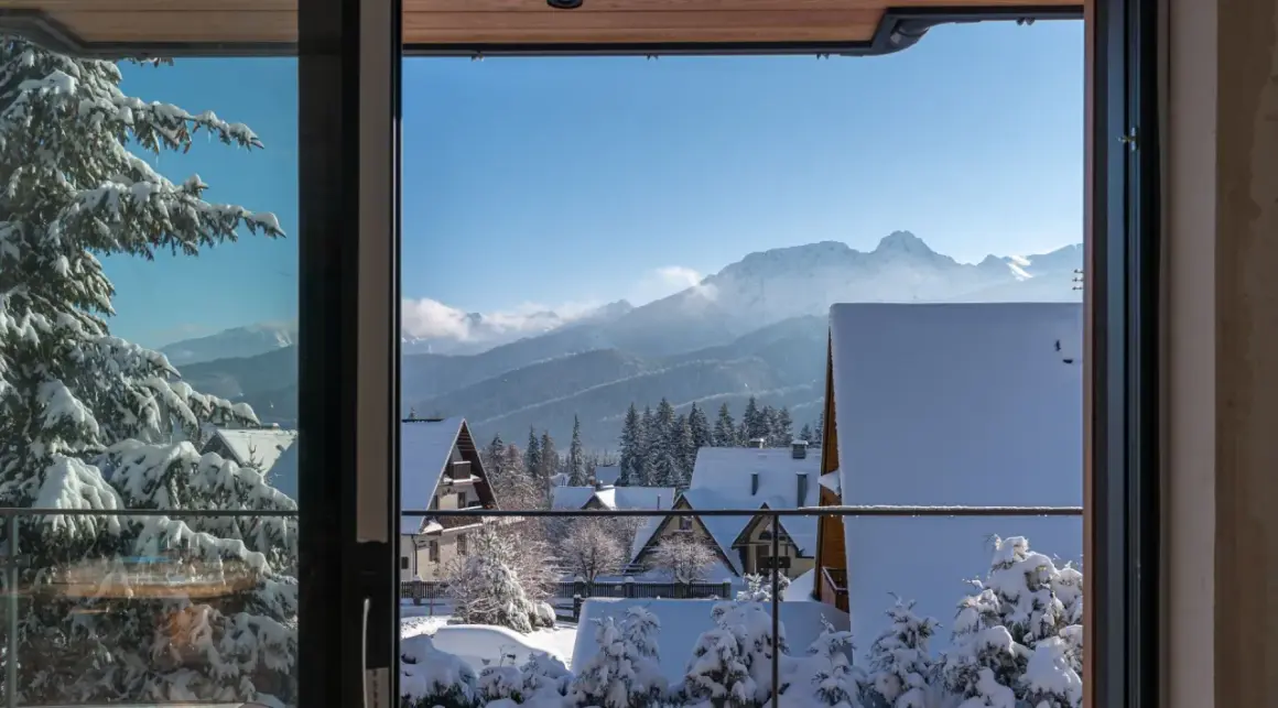 Zimowy krajobraz z ośnieżonymi domkami i lasem, idealny na nocleg z pięknym widokiem na Tatry.