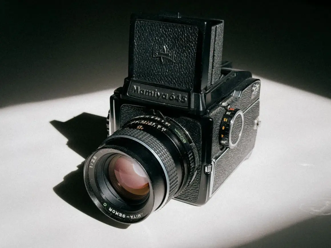 A classic Mamiya 645 medium format camera sits on a white surface, bathed in dramatic light and shadow.