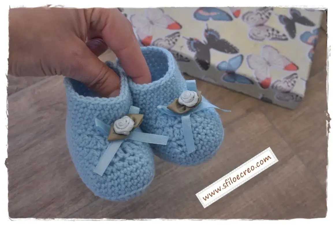 Delicate babbucce uncinetto azzurre, decorate con fiocchi e rose, perfette per un neonato. Trova schemi gratis per crearle!