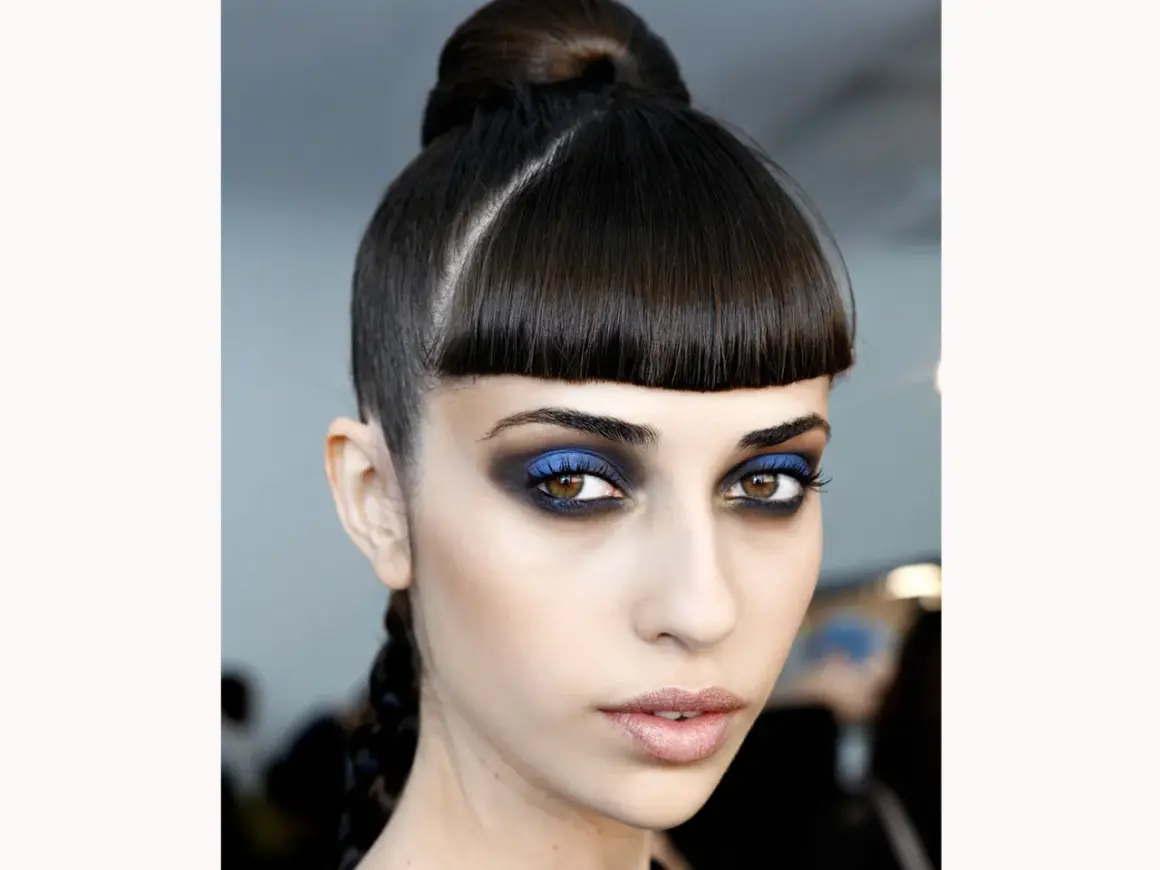 Occhi intensi con smokey eyes blu elettrico e nero, capelli raccolti in uno chignon e treccia.