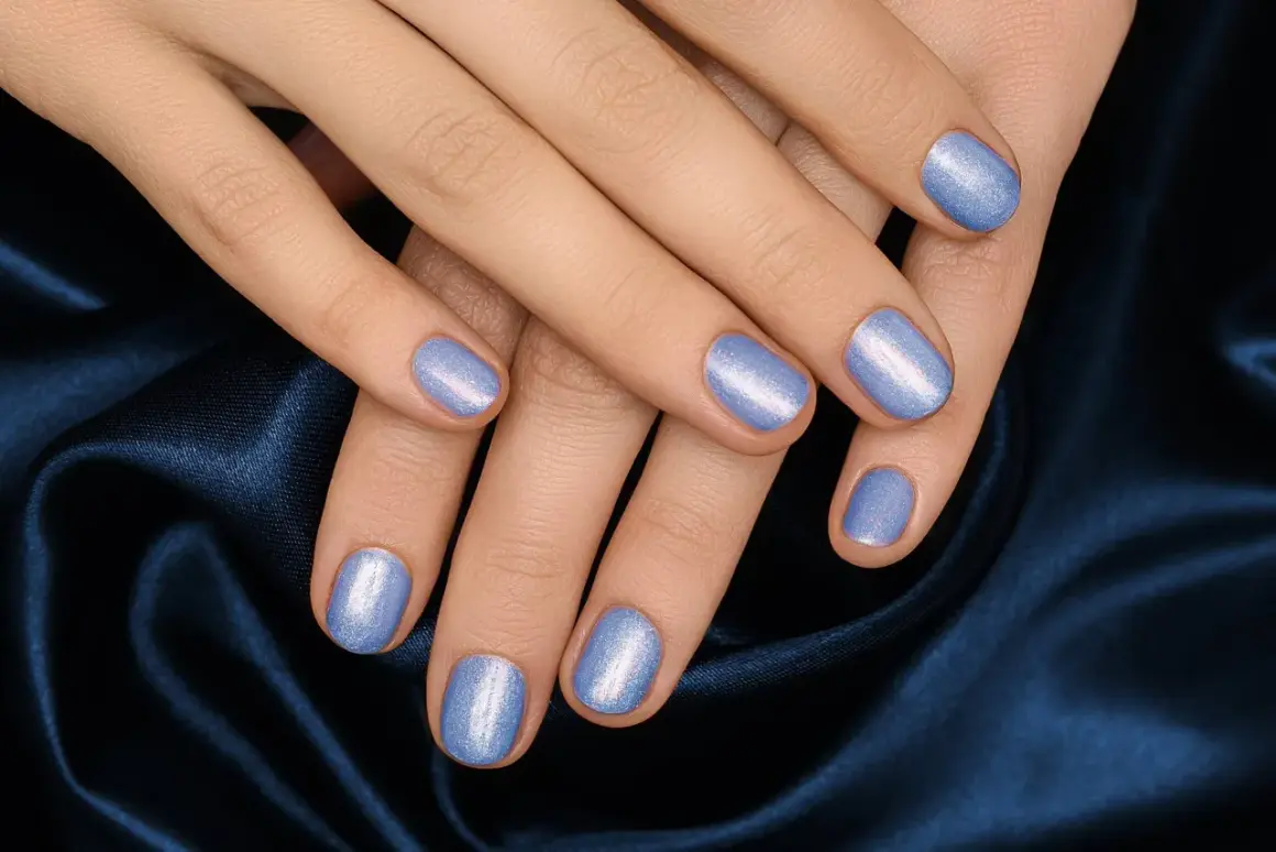 Mani curate con unghie corte rotonde smaltate di un azzurro perlato, adagiate su un tessuto blu notte.