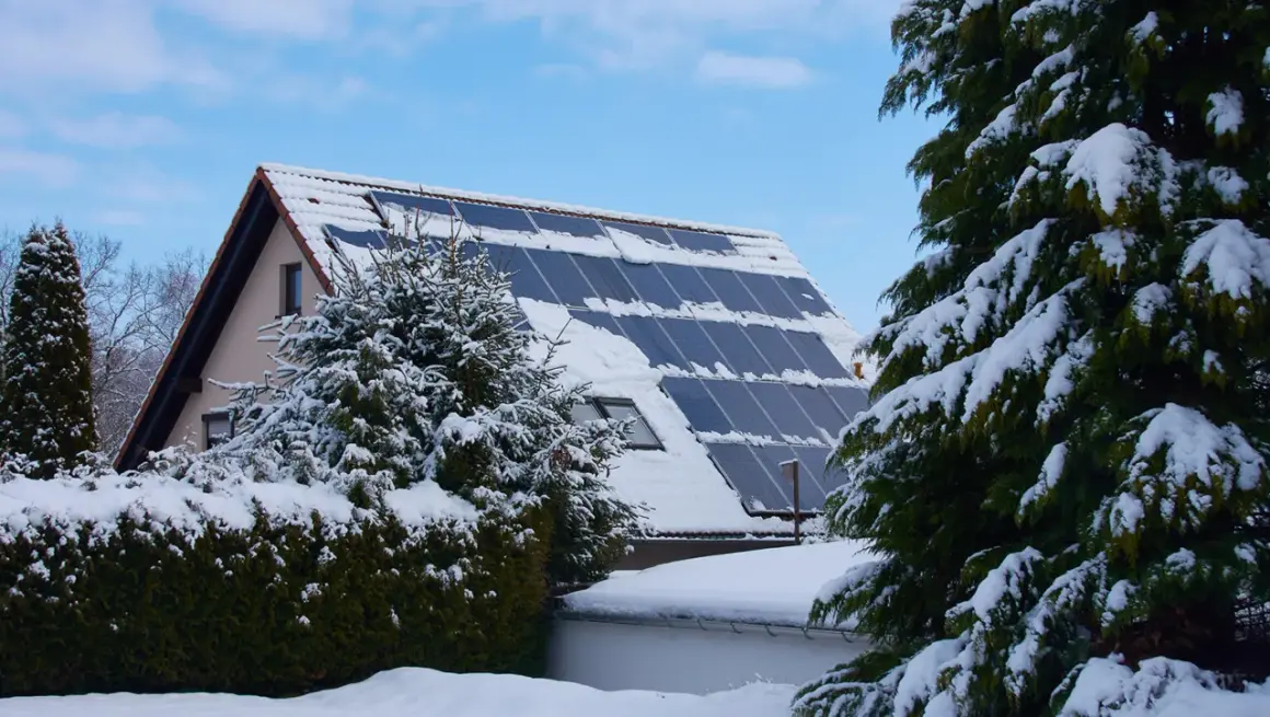 Schneebedeckte Solaranlage auf einem Hausdach, die zeigt, wie man im Winter heizen kann.
