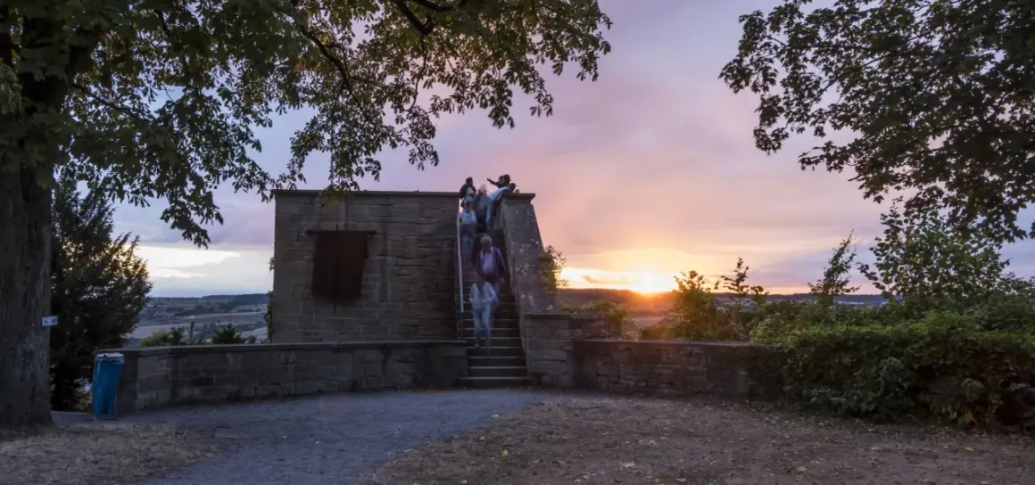 Menschen steigen die Treppen zum schlosskeller herrenberg hinauf, während die Sonne bei einem dramatischen Abendhimmel untergeht.