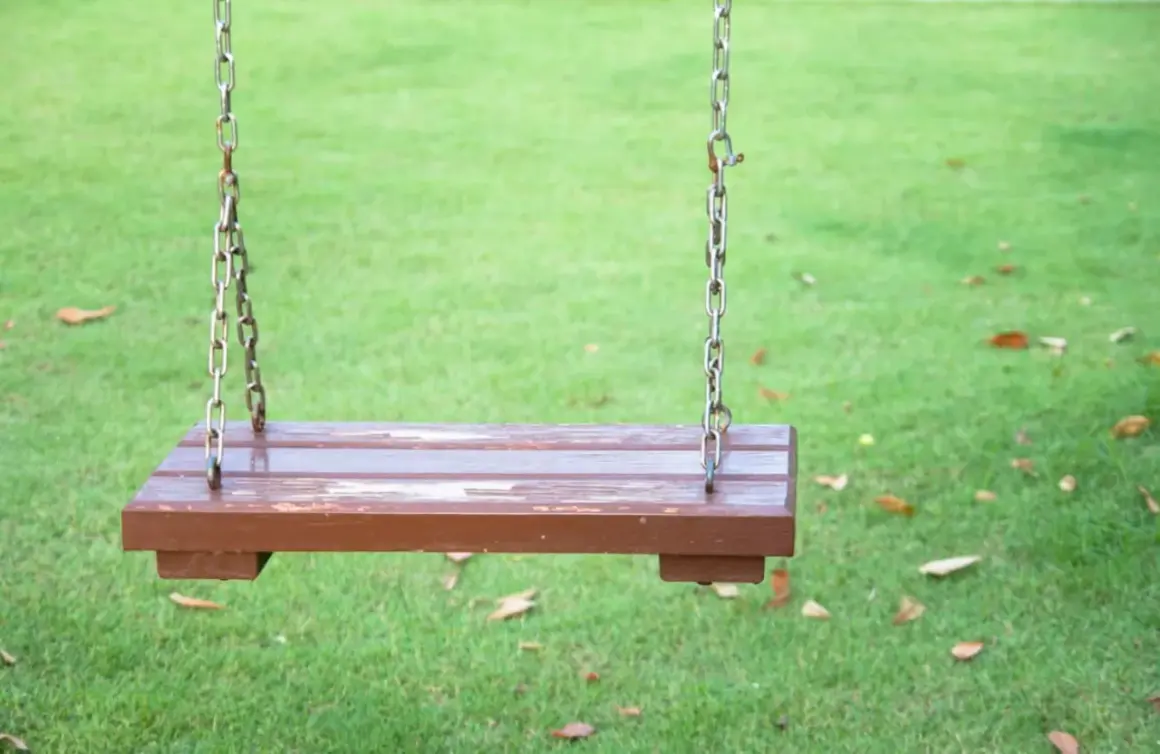 Prosty projekt: jak zrobić huśtawkę ogrodową z bali. Drewniane siedzisko na łańcuchach, gotowe do zabawy na trawie.