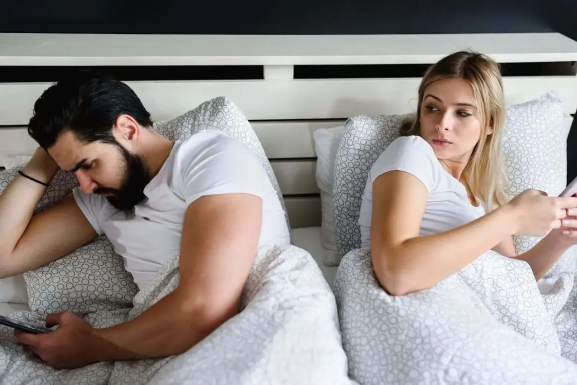 Ein Mann liegt im Bett und schaut auf sein Handy, während seine Frau ihn misstrauisch beobachtet. Er guckt vielleicht gerade Porno.