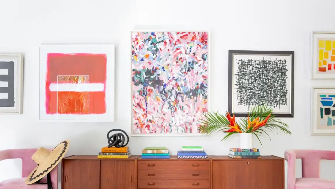 Vibrant abstract art and graphic prints adorn a wall above a midcentury credenza, showcasing a stylish blend of midcentury graphic design.