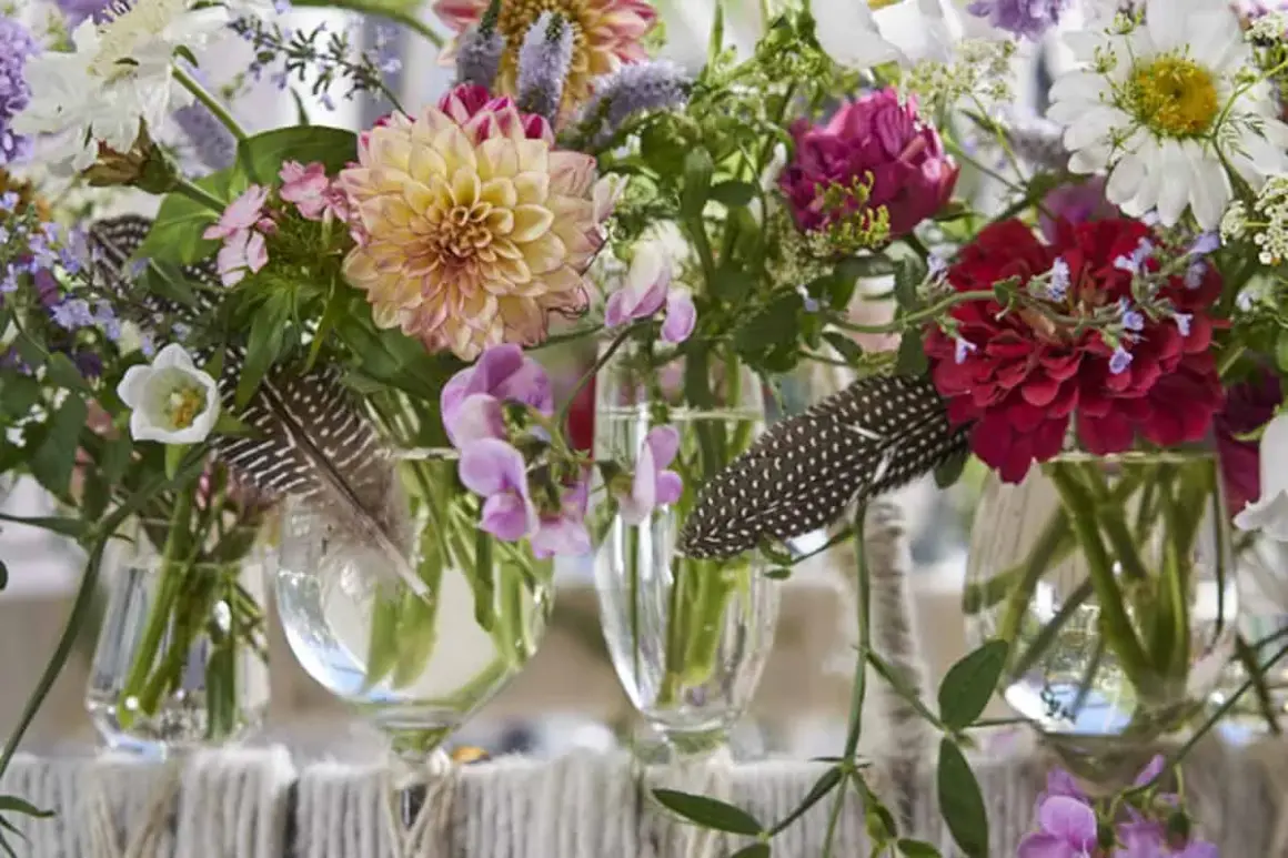 Moderne tischdeko blumen: Dahlien, Rosen und Margeriten in Glasvasen, dekoriert mit Federn.