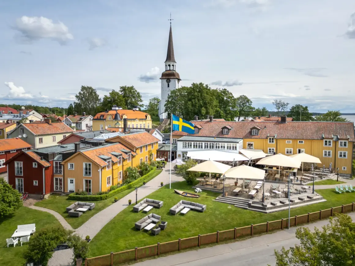 Mariefreds Värdshus med svensk flagga och kyrktorn. Uteservering med parasoller och sittgrupper i gräset.