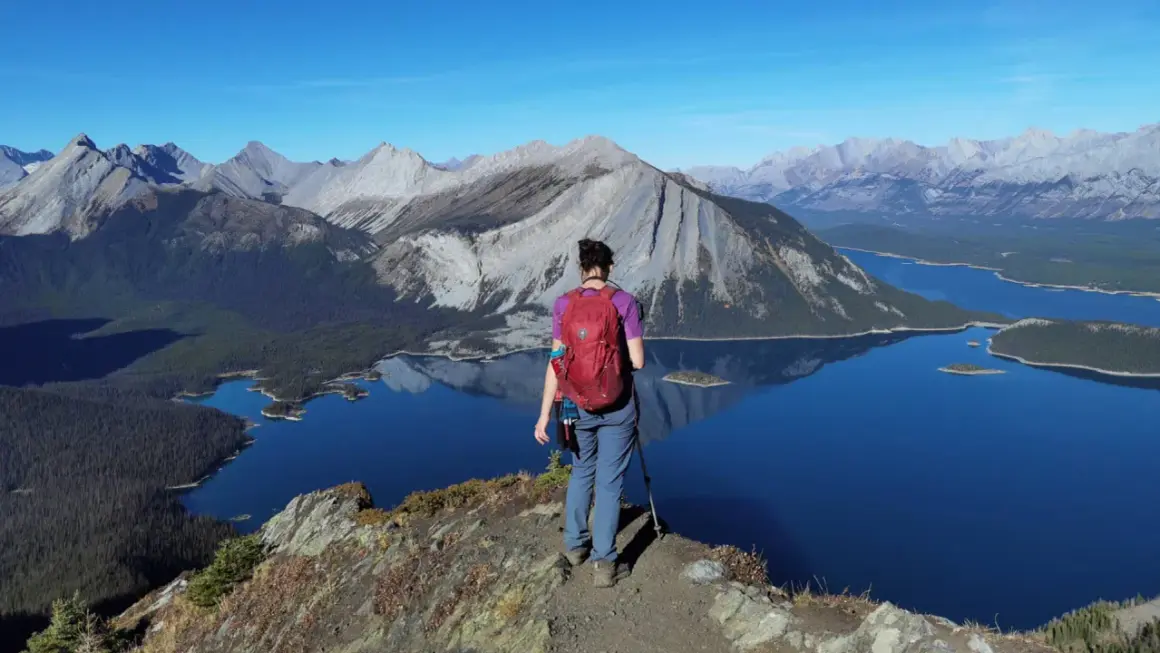 Senderista admira el paisaje montañoso y lagos turquesas, un ejemplo de qué ver en Canadá.
