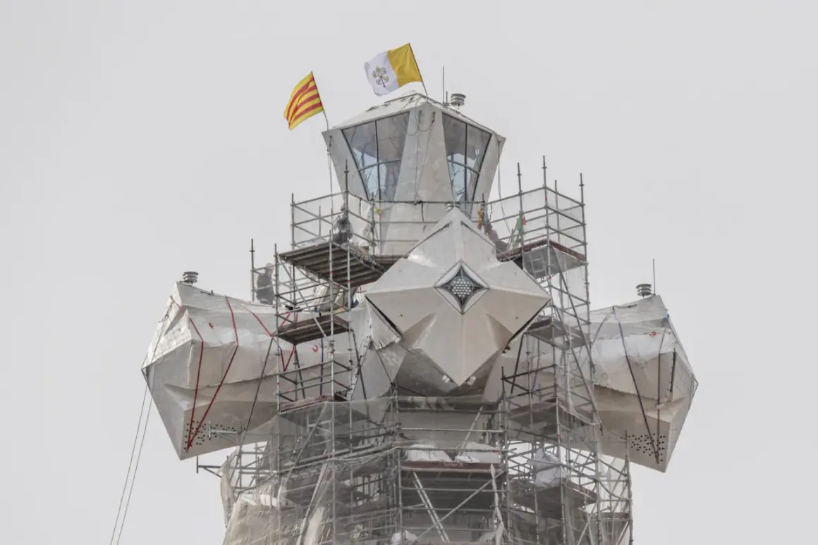 La torre de Jesús de la Sagrada Familia, cubierta con lonas y rodeada de andamios, ondea las banderas de Cataluña y el Vaticano.