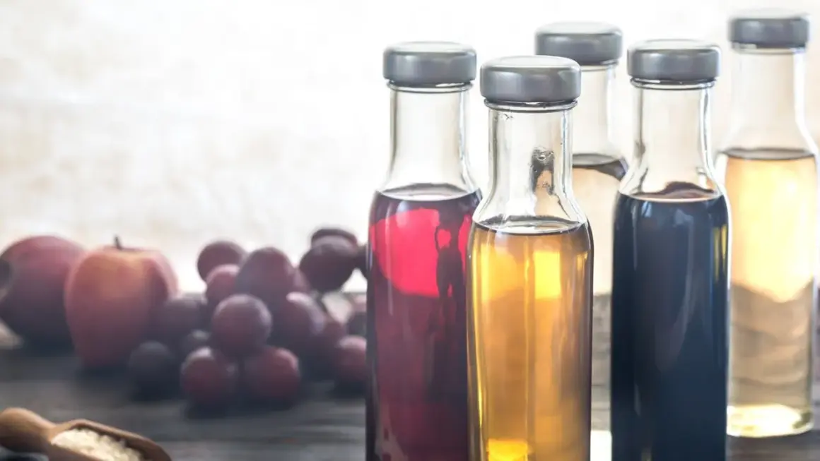 Flaschen mit verschiedenen Essigsorten, Äpfel und Trauben. Essigwasser gesund für den Körper.