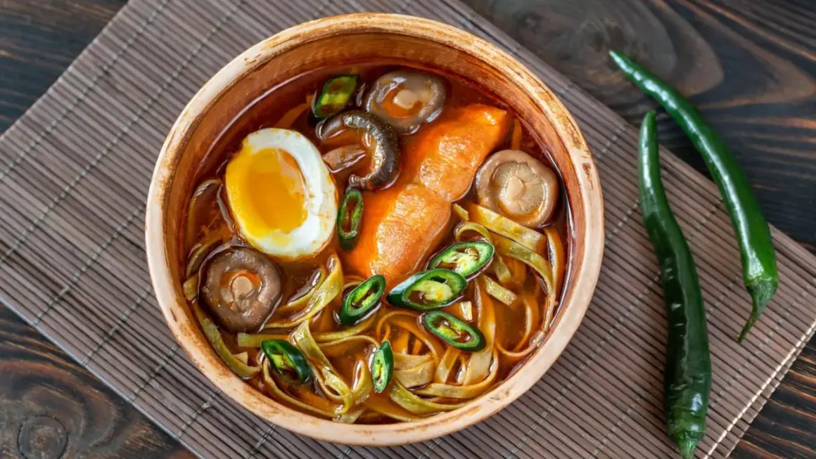 Eine Schüssel Ramen mit Ei, Pilzen und Chili. Der würzige Sud weckt die umami zunge und verspricht ein intensives Geschmackserlebnis.