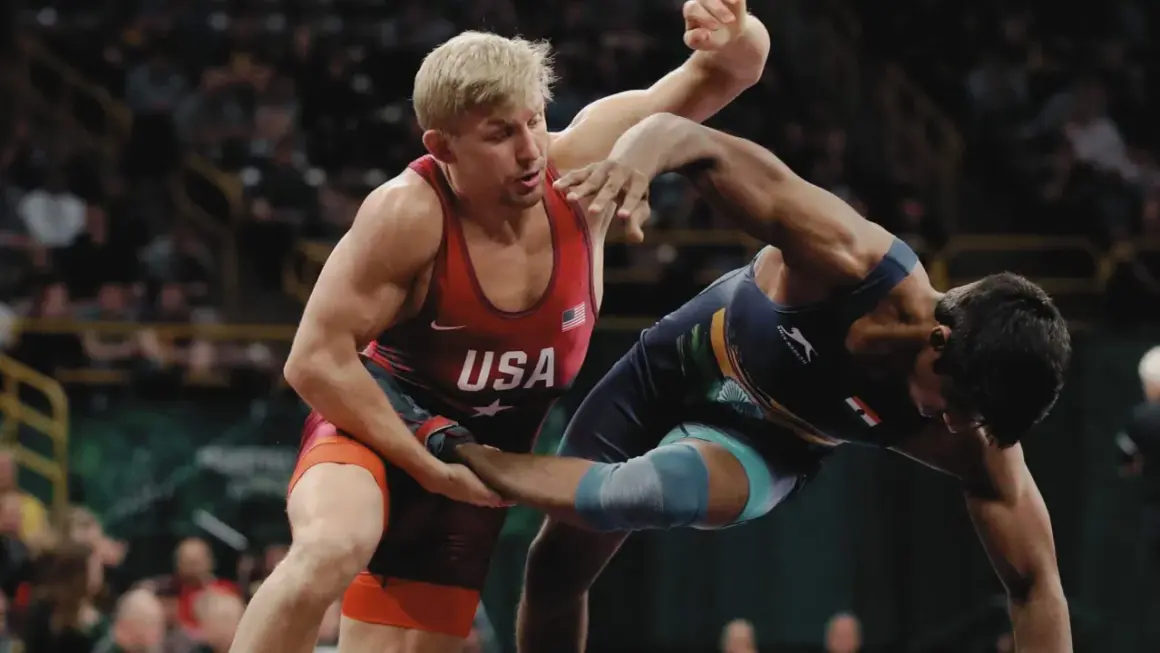 Två brottare i intensiv kamp. En bär USA:s färger, den andra en mörkblå dräkt. Spänningen är påtaglig i denna wrestling sverige-match.