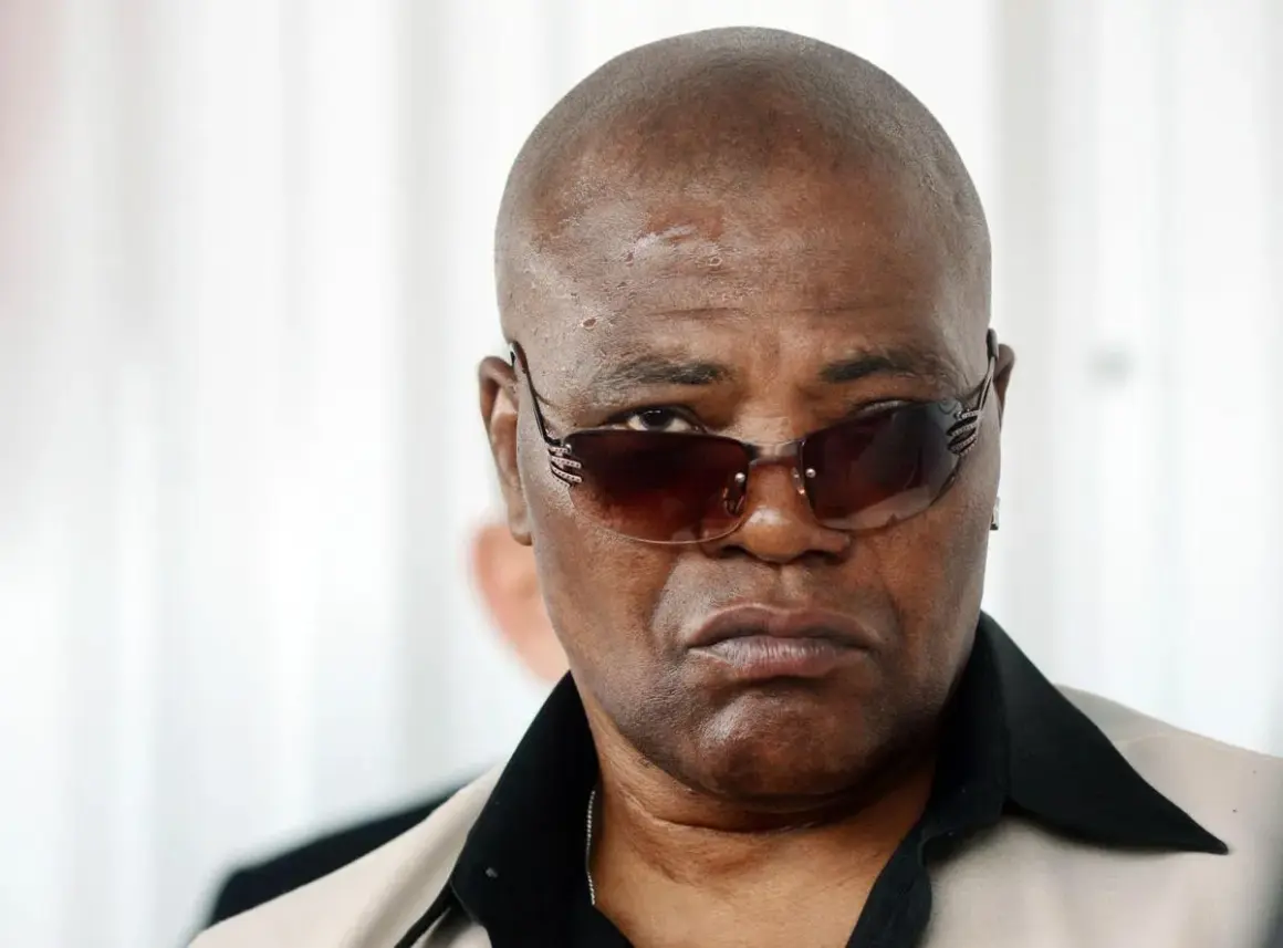 Arron Pryor, a man with a serious expression, wears stylish sunglasses and a light-colored jacket with a black collar.