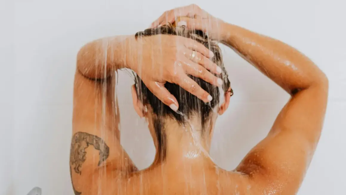 Frauenkopf unter der Dusche, Wasser rinnt über Schultern und Arme mit einem frischen Tattoo.