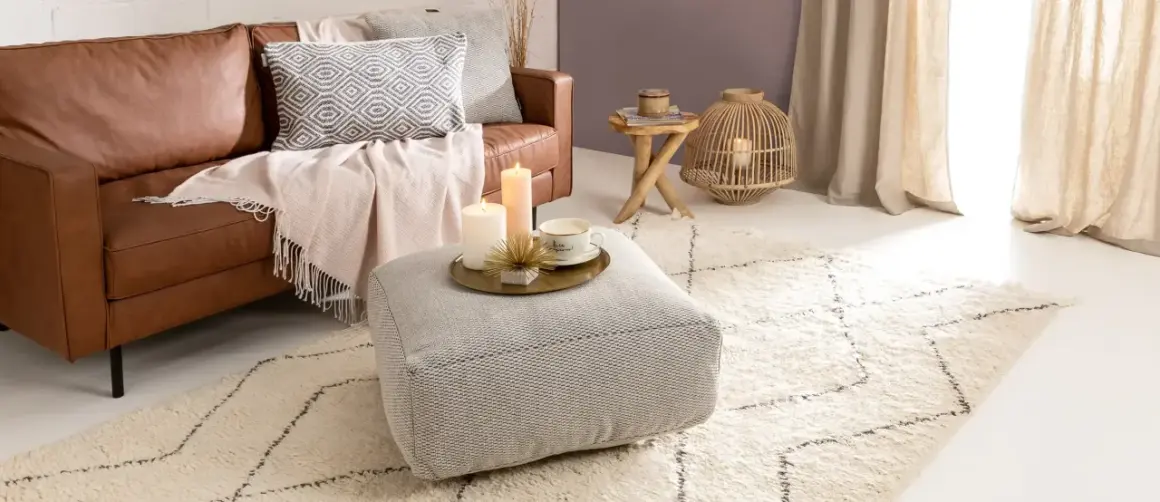 Gemütliches Wohnzimmer im hygge stil mit Ledersofa, Kissen, Decken, Kerzen und einem Teppich.