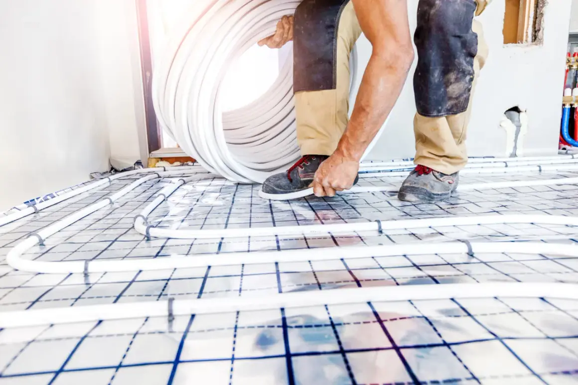 Worker installing underfloor heating pipes on a grid system.