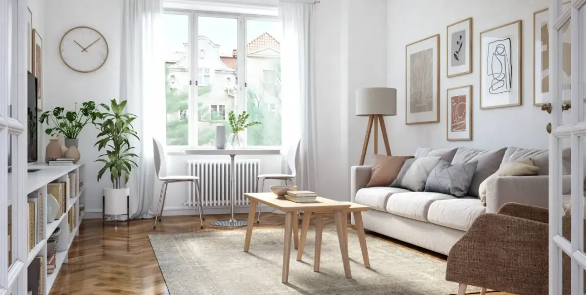 Ein helles Wohnzimmer mit Sofa, Couchtisch, Bücherregal und Pflanzen. Kunstwerke zieren die Wand, während durch das Fenster Tageslicht einfällt.