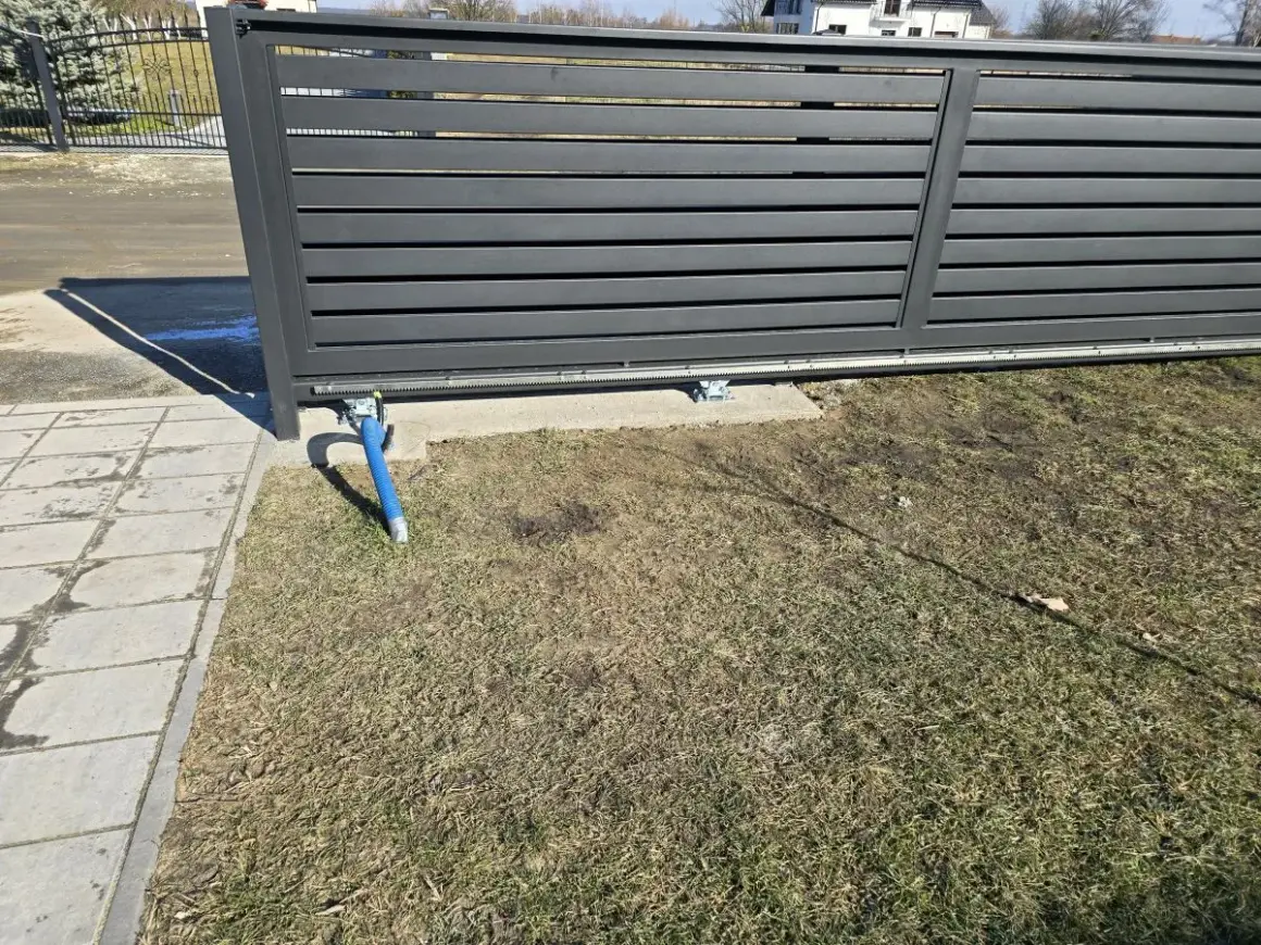 Widoczny mechanizm bramy przesuwnej, z wózkami podtrzymującymi. Jaki rozstaw wózków do bramy przesuwnej jest kluczowy dla płynnego działania.