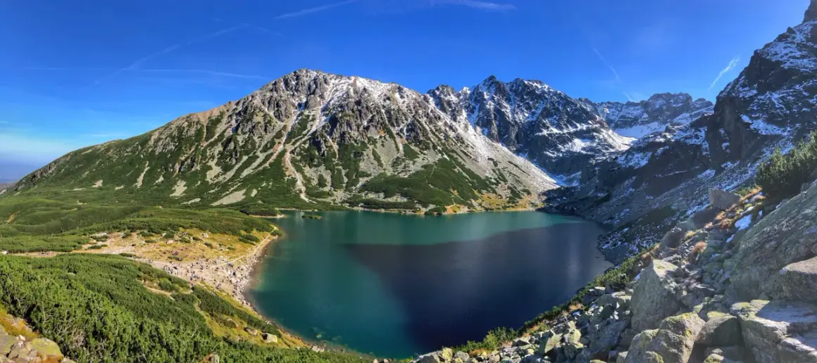Piękne Tatry dla początkujących: Morskie Oko otoczone zielenią i ośnieżonymi szczytami. Tłumy turystów podziwiają widok.