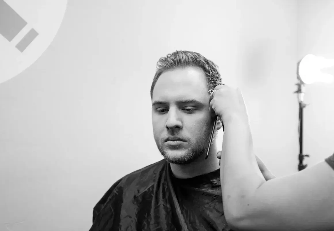 Un uomo con barba e basette viene tagliato. Diverse tipi di basette sono possibili, ma queste sono in fase di definizione.
