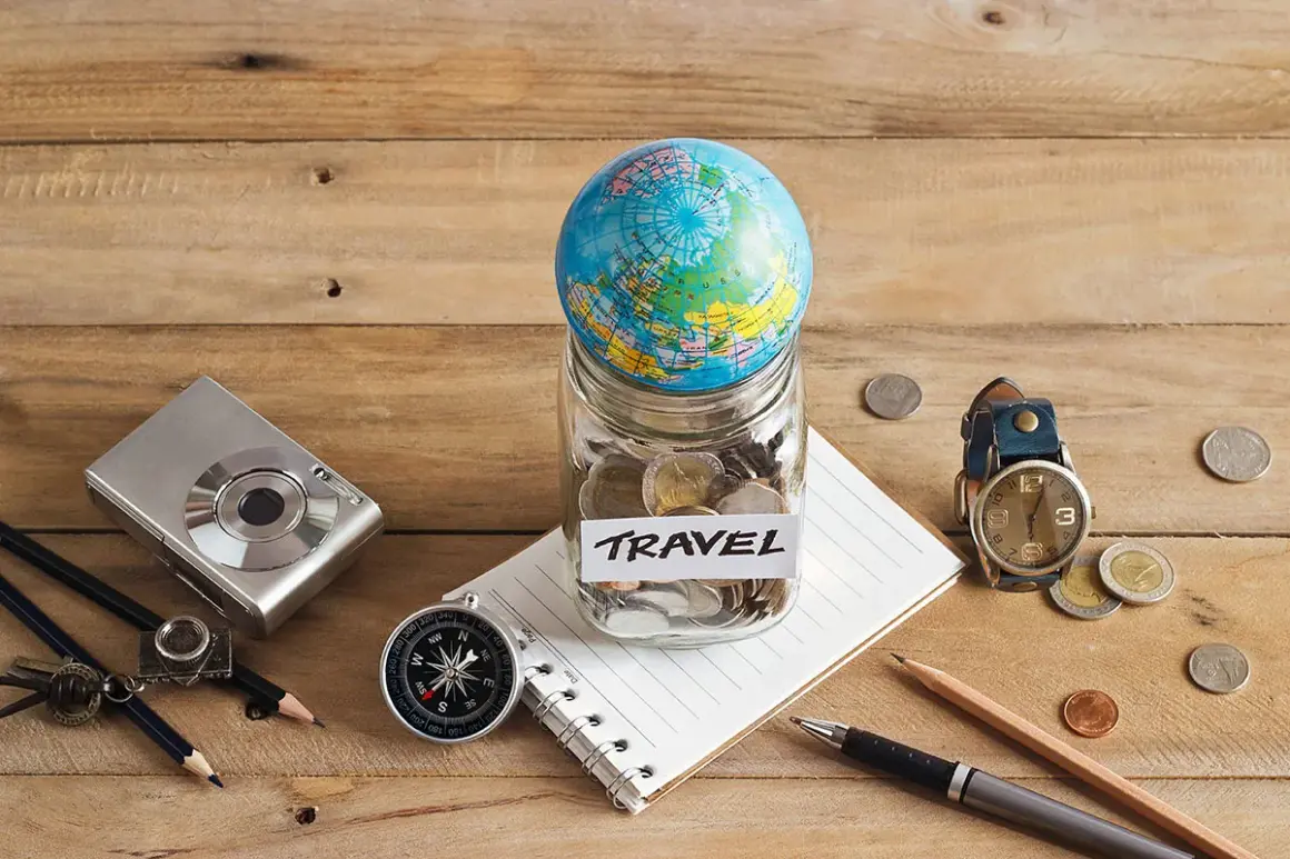 Bocal rempli de pièces avec un globe, un appareil photo, une boussole et un carnet, prêt pour le backpacking en Europe.