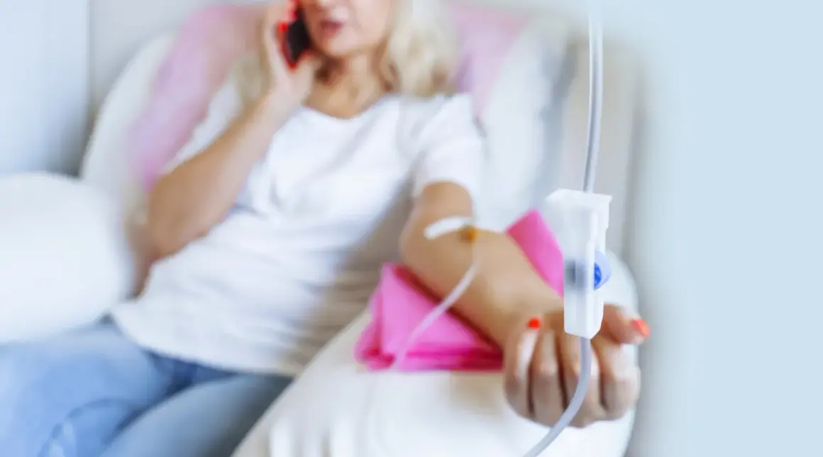 Frau erhält Infusion, während sie telefoniert. Thema: Brustkrebs HER2 und Lebenserwartung.