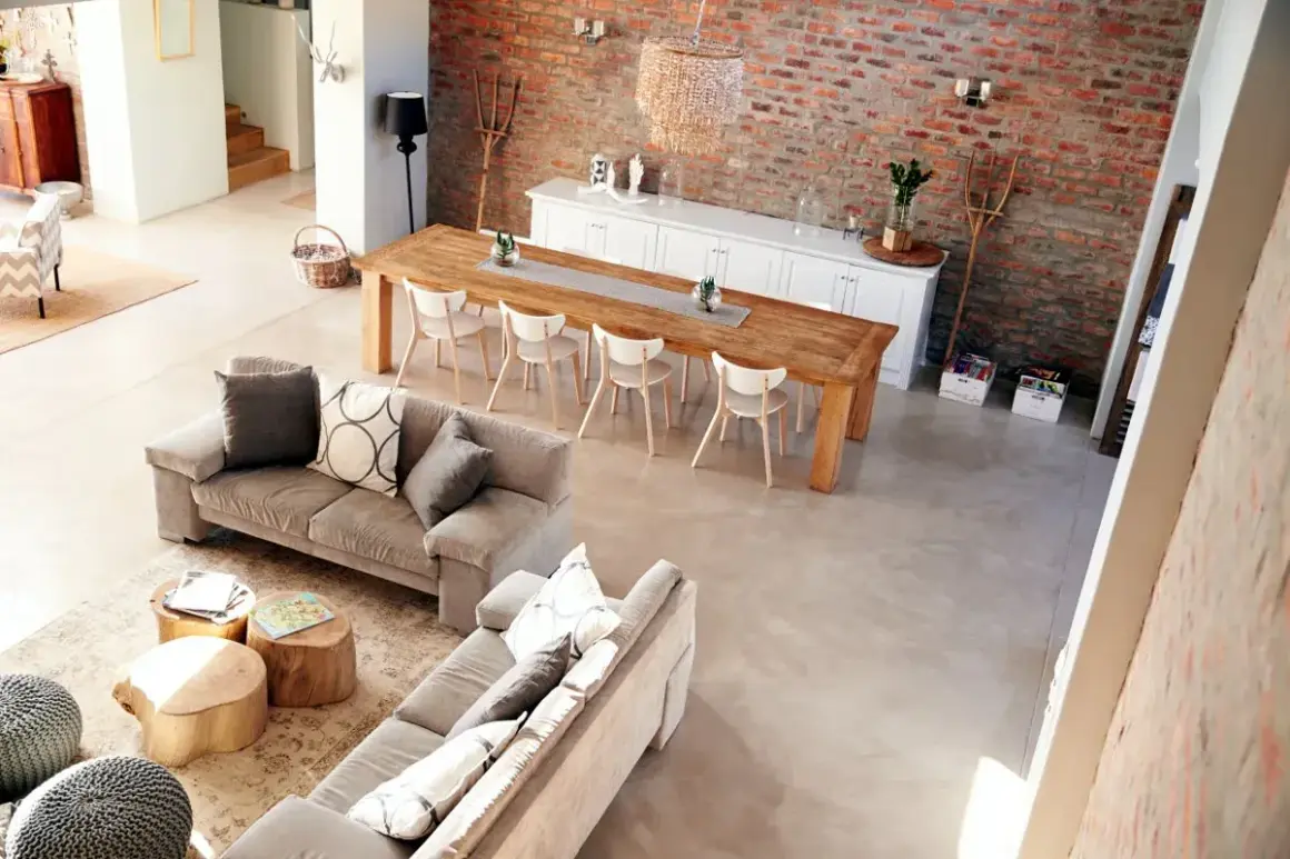 Nowoczesny salon w stylu rustykalnym z ceglaną ścianą, drewnianym stołem i wygodnymi sofami.