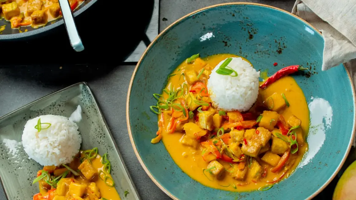 Ein köstlicher Thai Curry mit Tofu, Gemüse und Reis, garniert mit Frühlingszwiebeln und Chili.