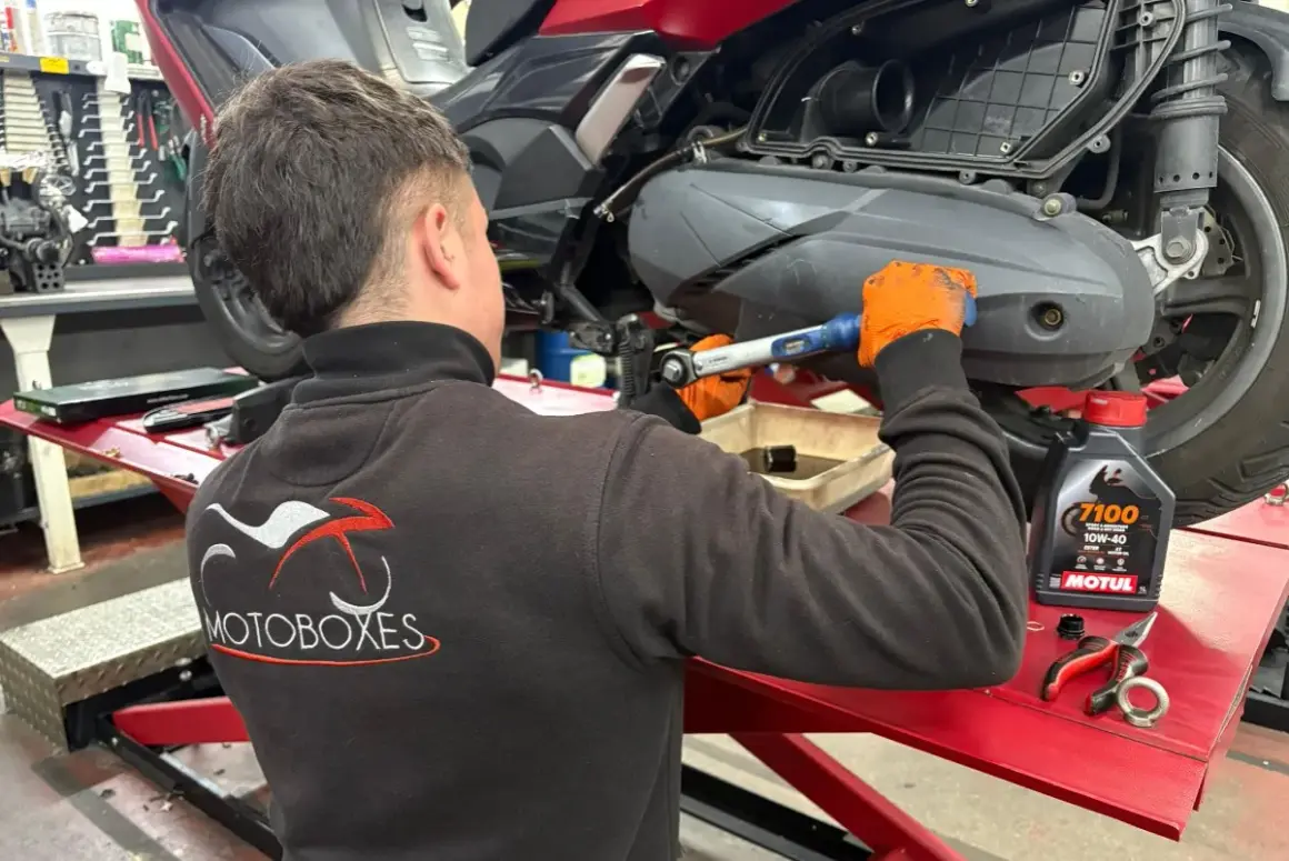 Mecánico con guantes naranjas realiza cambio de aceite a moto. Consulta el precio del cambio de aceite de moto y el aceite Motul.