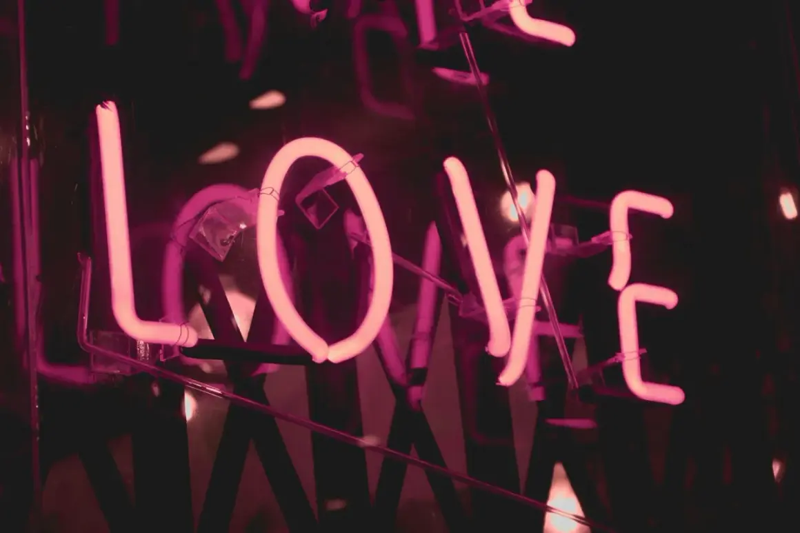 Lettere al neon rosa formano la parola "LOVE", un invito a dedicare una canzone per una persona speciale in italiano.