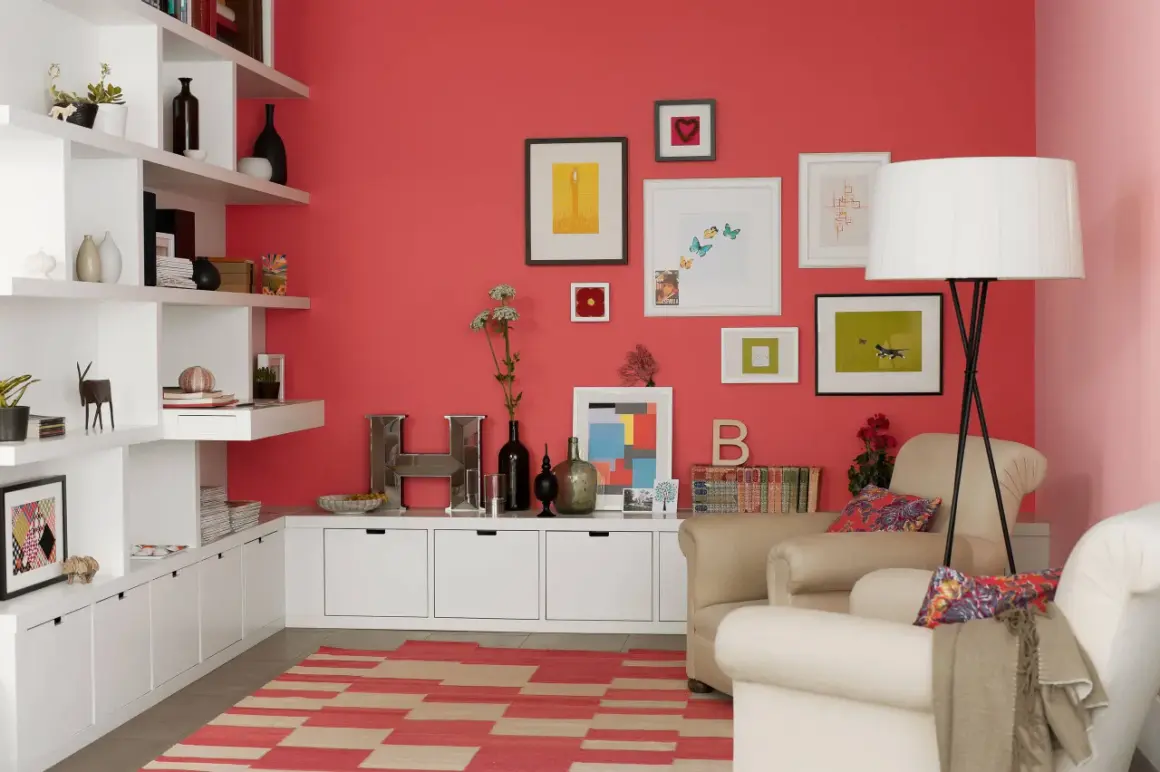 Wohnzimmer mit koralle farbener Wand, weißen Regalen, beigefarbenen Sesseln und einem Teppich mit roten und beigen Streifen.