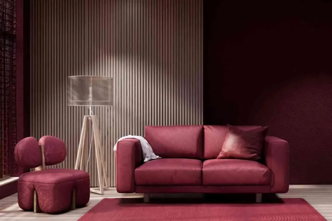 Divano e poltrona in velluto color bordeaux, con tappeto e parete coordinati. Lampada da terra con paralume trasparente.