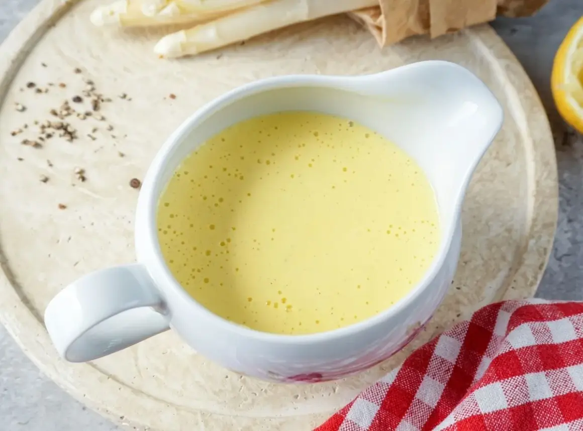 Cremige Sauce Hollandaise in einer Sauciere, daneben Spargel und Zitronenspalte. Perfekt für ein Frühlingsgericht.