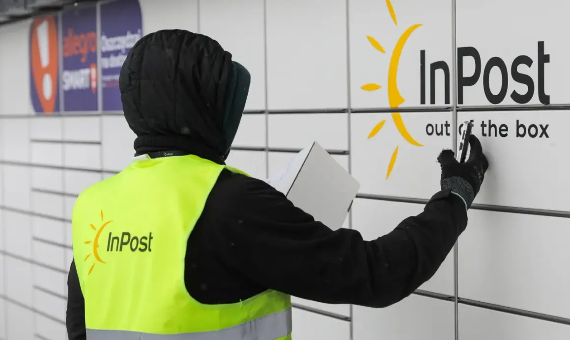 Pracownik w kamizelce InPost z paczką przy paczkomacie. Czy muszę naklejać etykietę InPost? Nie, wystarczy kod nadany przez system.
